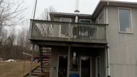 2-story house with upper wooden deck and stairs leading up to it